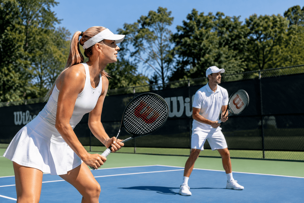 Nainen ja mies pelaamassa tennistä Wilson-tennismailoilla ulkokentällä.